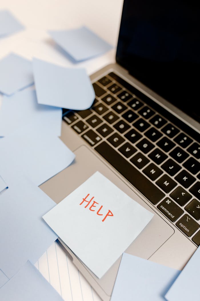 A laptop covered with sticky notes and a prominent "Help" sign, conveying urgency.